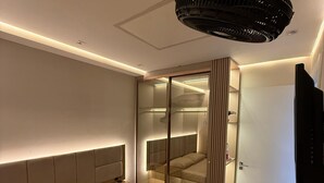Ein modernes Hotelzimmer mit einem großen Bett, einem verglasten begehbaren Kleiderschrank, einem Deckenventilator und einem flachbildfernseher an der Wand.