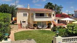 Una casa de dos pisos con un balcón, un pequeño jardín y un patio con mobiliario exterior.
