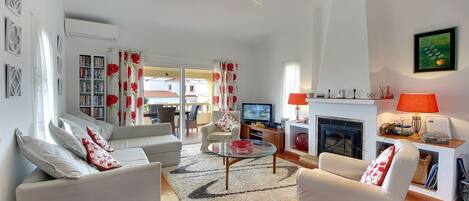 A living room with a sofa set, a glass coffee table, a fireplace, and a bookshelf.