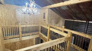 A wooden interior with a central wooden staircase, a chandelier, and a metal railing.