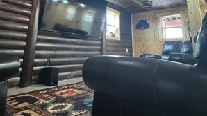 A log cabin interior with a large TV, leather sofa, and a patterned rug. - Rustic Barndominium Retreat (Pleasanton)