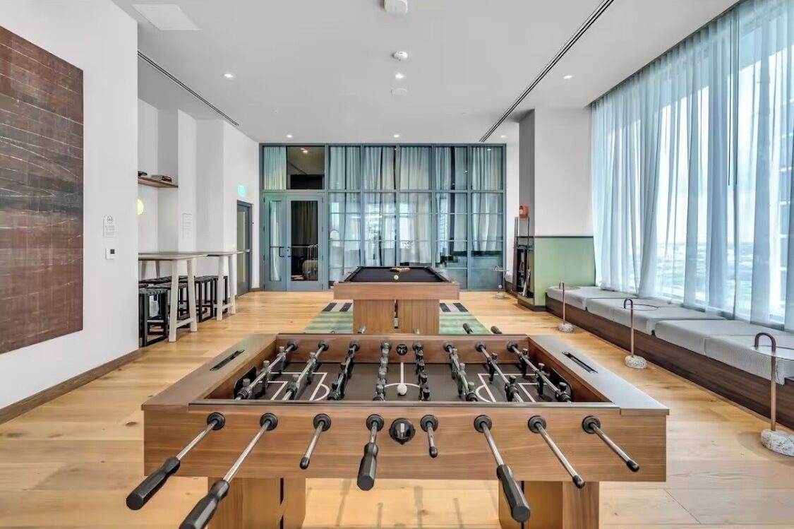 A modern indoor space with a foosball table, seating area, and large windows.