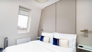 A modern hotel room with a large bed, a small window, a radiator, and a chair. - Impressive South Kensington Central Apartment (London)