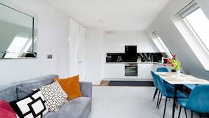 A modern apartment with a dining area, kitchenette, and a large window providing natural light. - Impressive South Kensington Central Apartment (London)
