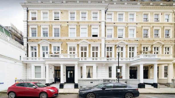 A row of three-story townhouses with a symmetrical facade, white and yellow brickwork, and a central entrance with a black door. - Impressive South Kensington Central Apartment (London)