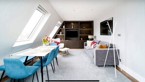 A modern living room with a dining area, a grey sofa, blue chairs, and a TV mounted on the wall. - Impressive South Kensington Central Apartment (London)