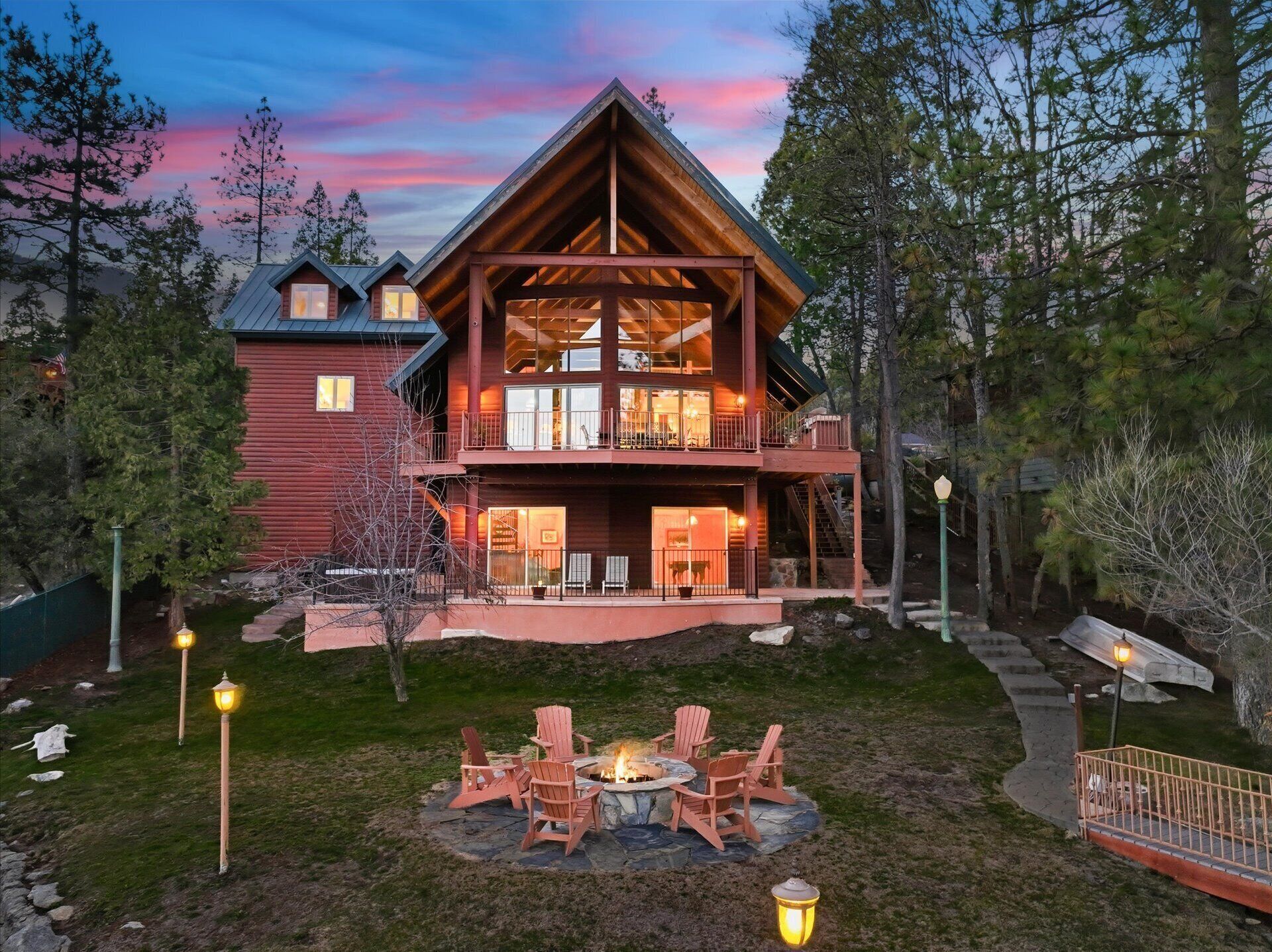 A two-story log cabin with a balcony, a stone fire pit, and outdoor seating.