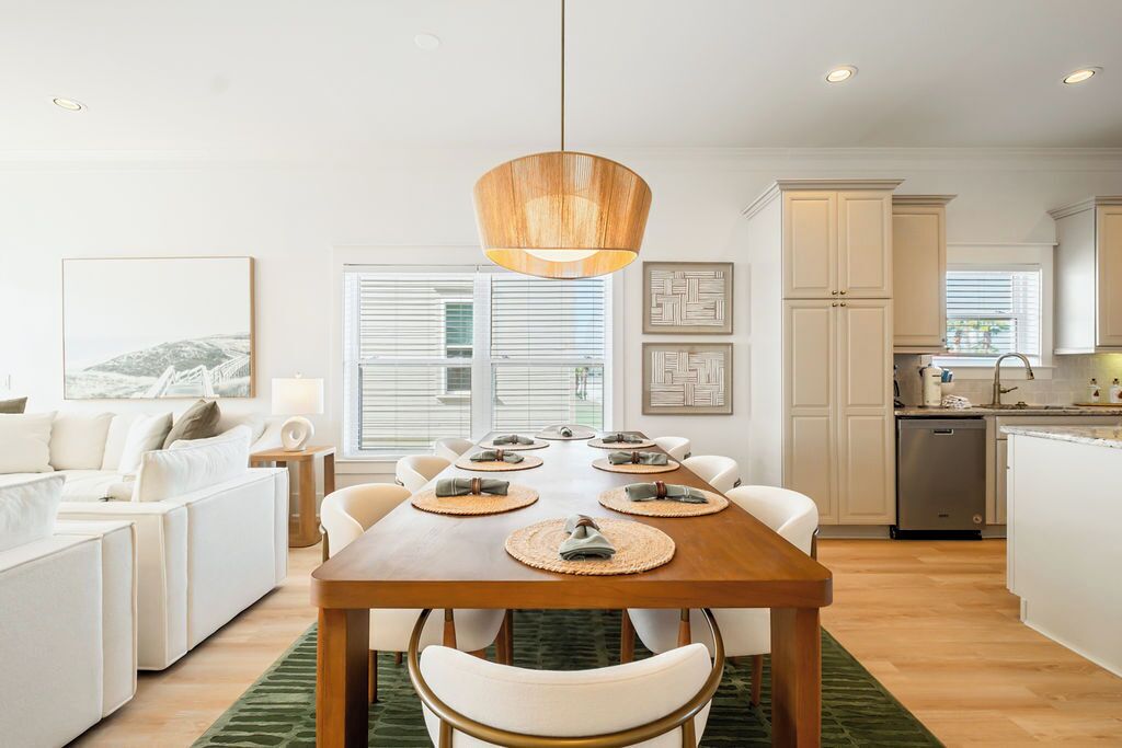 A modern kitchen with white cabinets, a wooden dining table set for six, and a hanging pendant light.