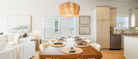 A modern kitchen with white cabinets, a wooden dining table set for six, and a hanging pendant light.