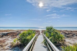 Ein hölzerner Steg führt zu einem Strand mit blauem Himmel und Blick auf das Meer.