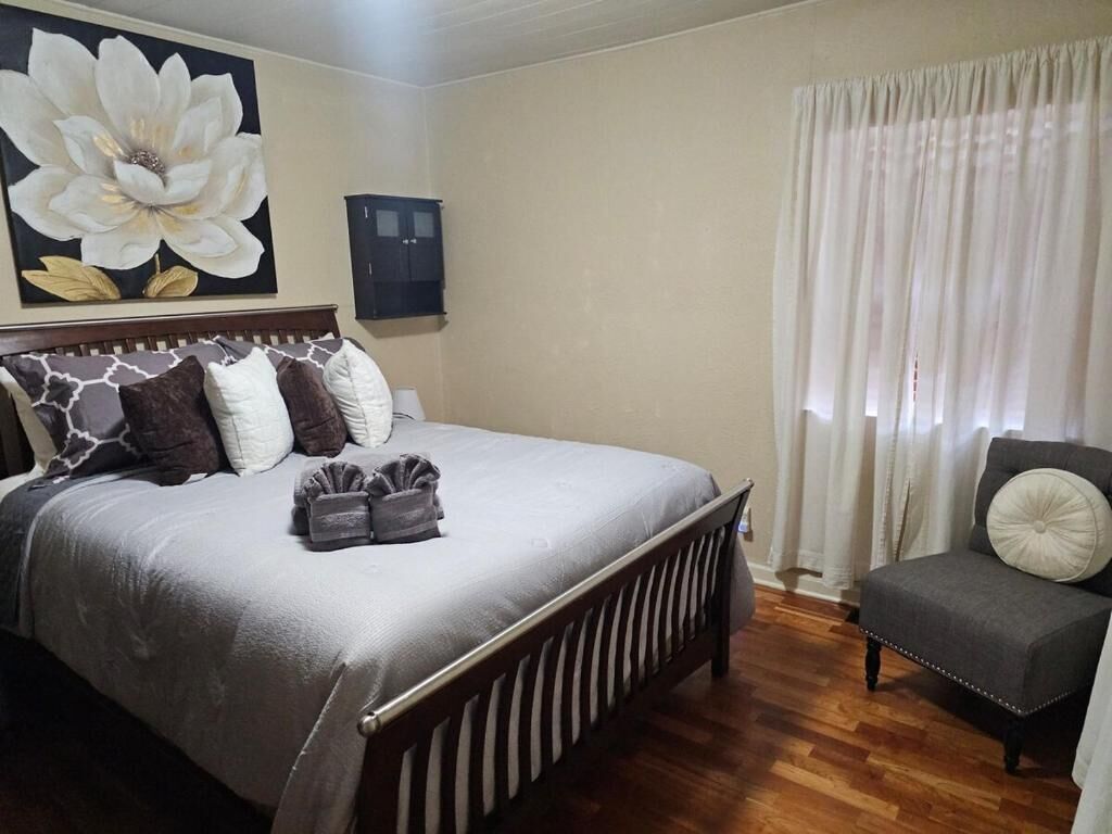 Een slaapkamer met een groot bed, een stoel, een schilderij en een kast.