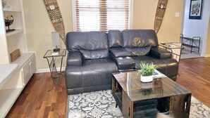 Ein Wohnzimmer mit einem dunkelbraunen Ledersofa, einem Glastisch mit Pflanze und einem Teppich mit Muster.