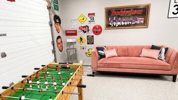 Ein Zimmer mit einem Fußballtisch, einem rosa Sofa und verschiedenen Wanddekorationen, darunter ein Budweiser-Schild und ein 'ONE WAY'-Schild.