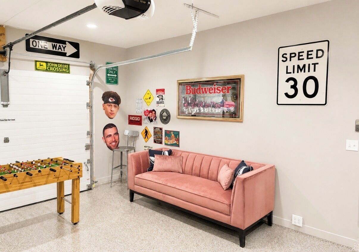 Una habitación con un sofá rosa, una mesa de fútbol de mesa y varios adornos en las paredes, incluyendo una señal de límite de velocidad y un cartel de Budweiser.