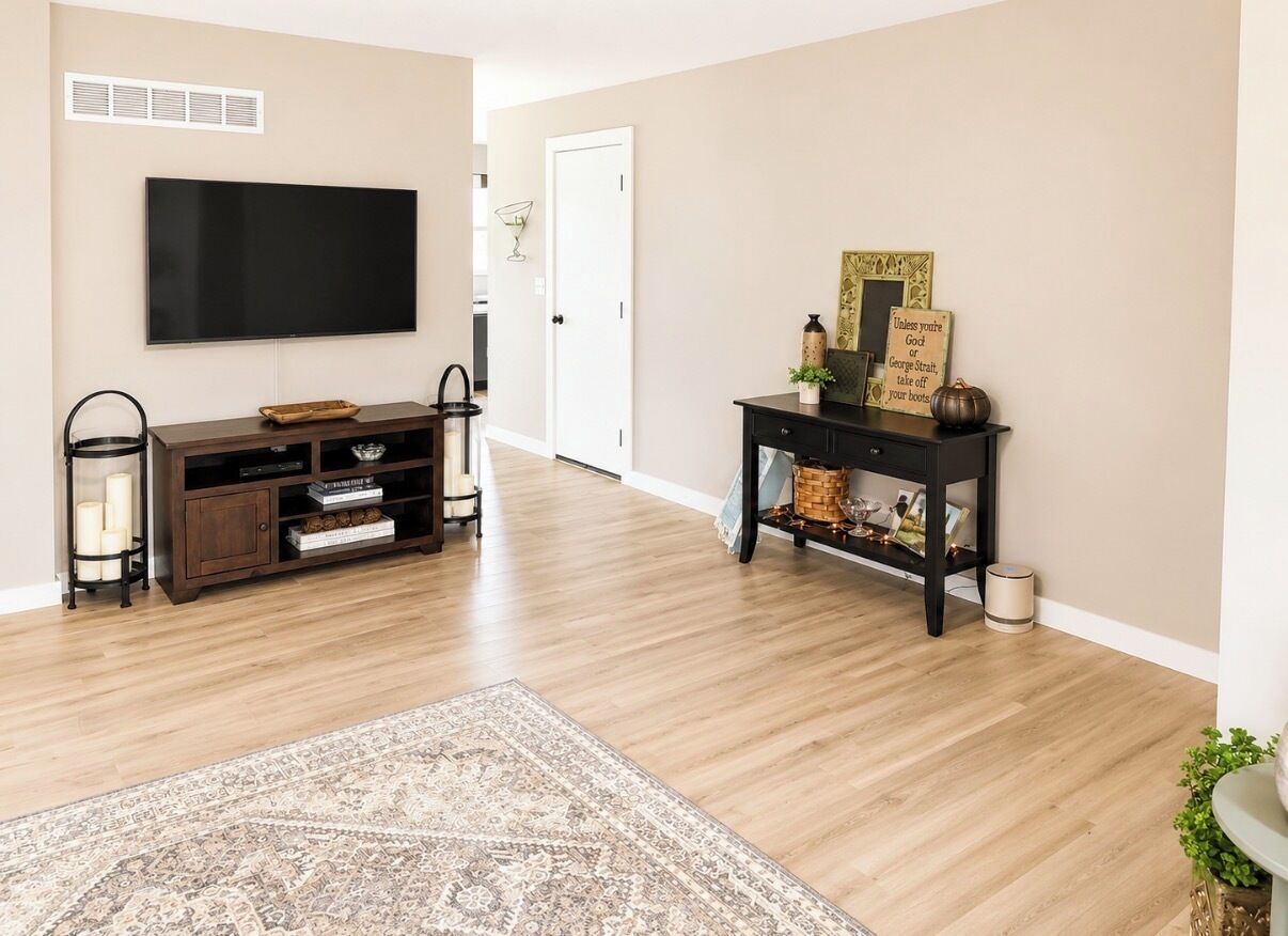 Een woonkamer met een flatscreen-televisie, een donkere houten entertainmentkast en een console tafel met decoratieve objecten.