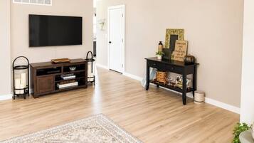Een woonkamer met een flatscreen-televisie, een donkere houten entertainmentkast en een console tafel met decoratieve objecten.