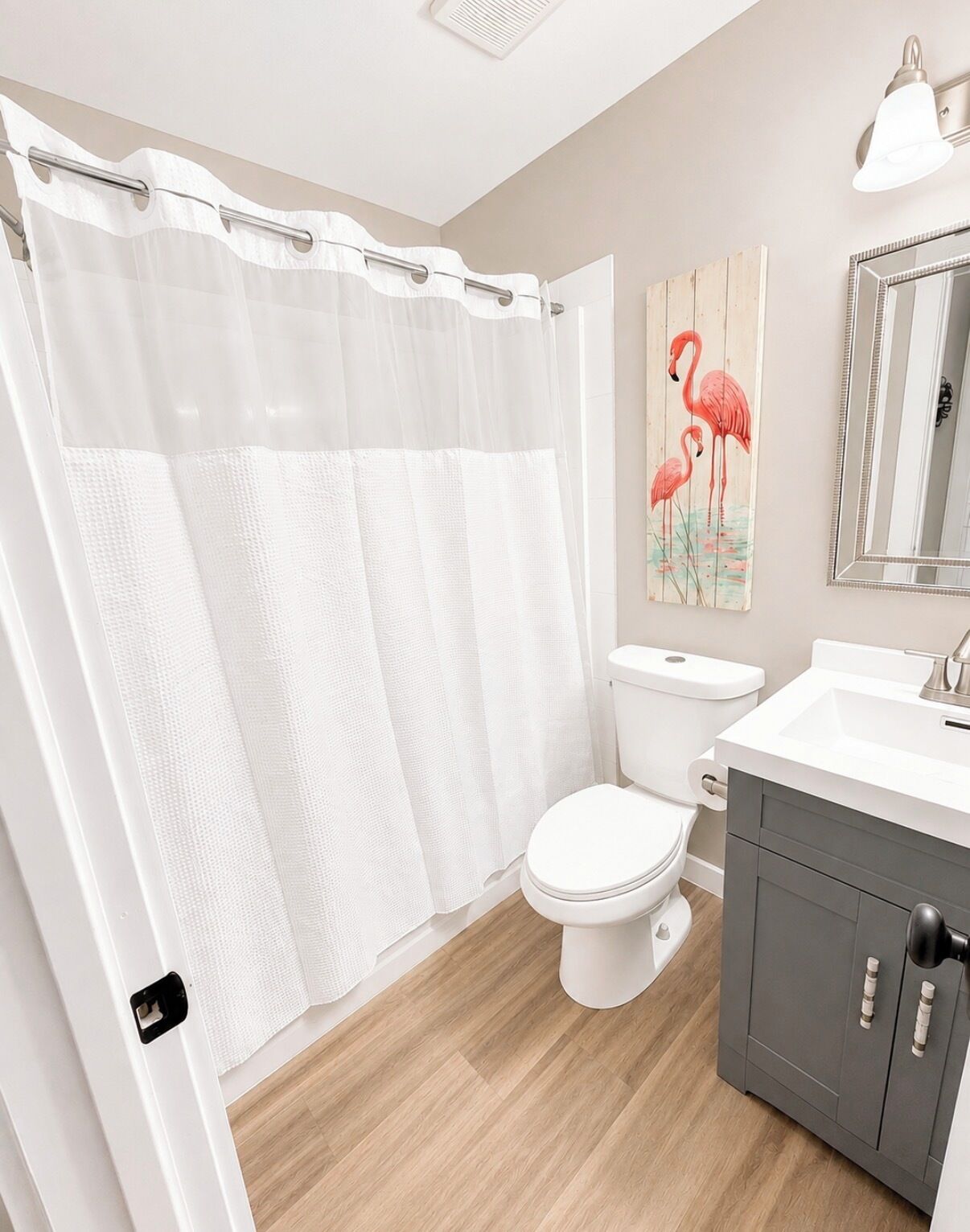 A bathroom with a shower curtain, toilet, sink, cabinet, and a mirror.