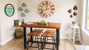En matplats med ett träbord, svarta metallstolar, en väggklocka, dekorativa fiskmotiv på väggen och en liten krukväxt.