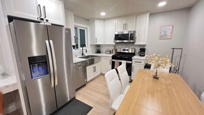 A modern kitchen with stainless steel appliances, white cabinetry, and a wooden dining table. - Modern El Cajon Retreat | Near SDSU and Zoo (El Cajon)