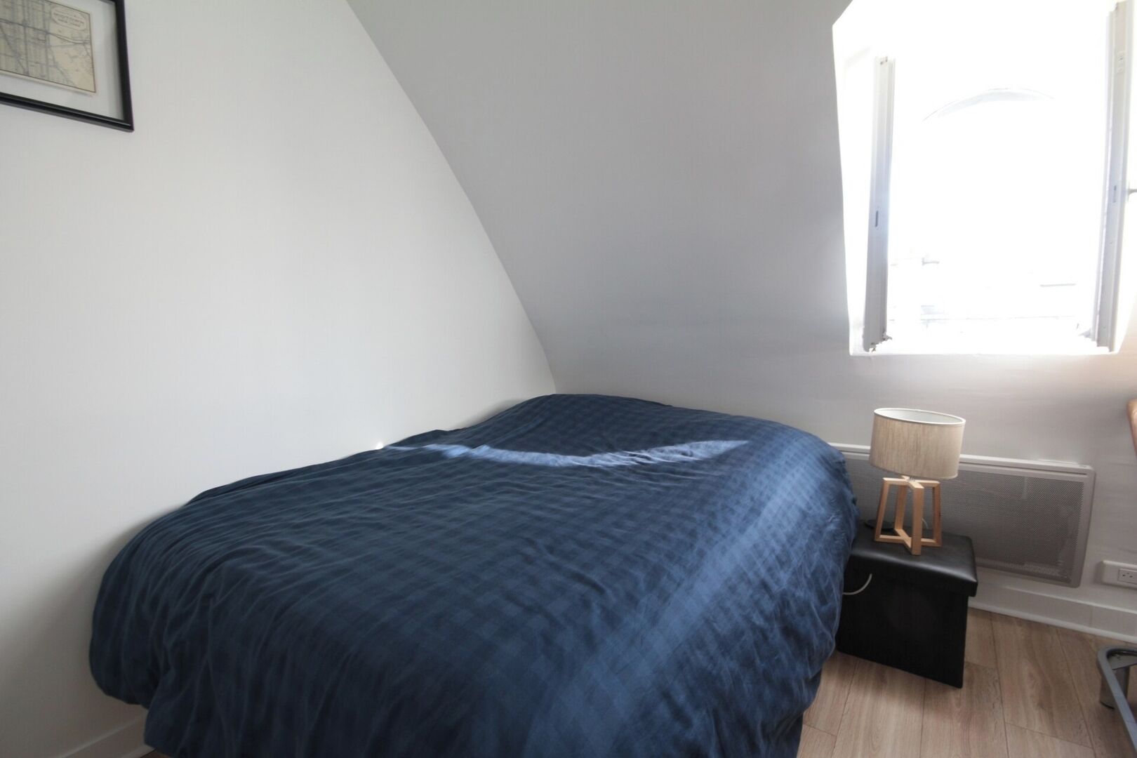 Un dormitorio con una cama, una mesita de noche, una lámpara y una ventana.
