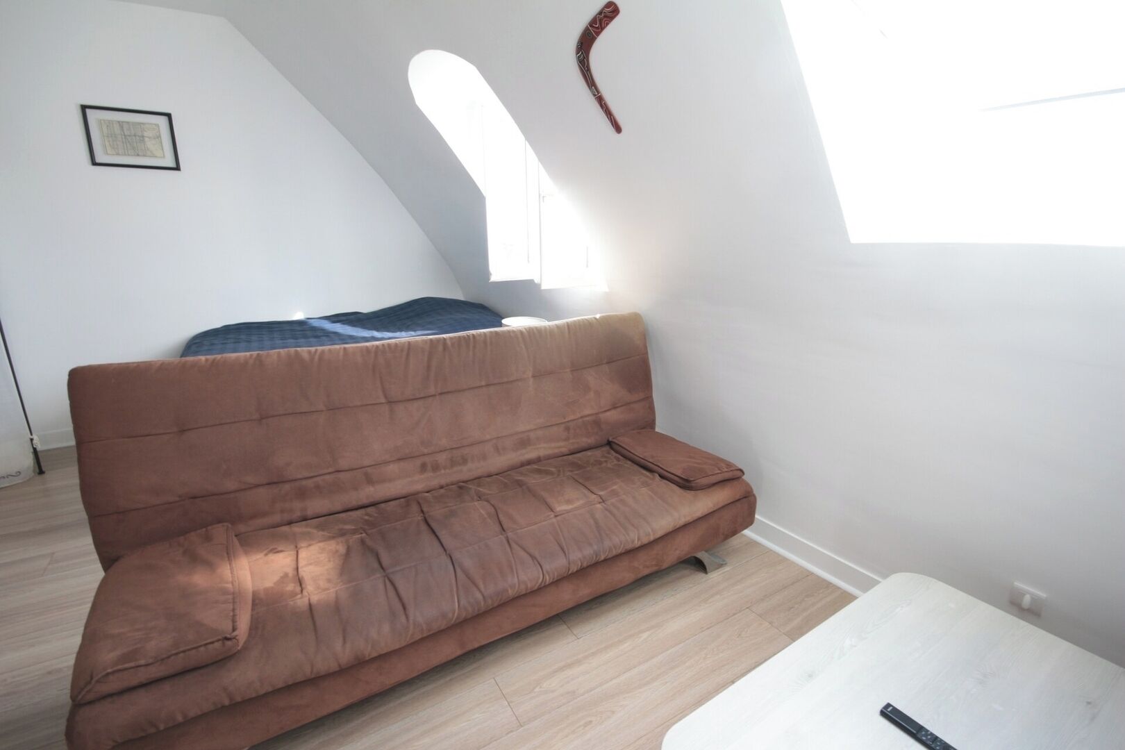 A room with a brown sofa, a white table, and a window with natural light.