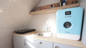 A kitchen with a blue appliance, a sink, a cutting board, and a shelf with jars. - Top floor studio and view - La Fayette / Opéra (Paris)