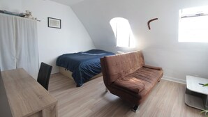 A compact bedroom with a bed, a brown sofa, a wooden table, and a small desk. - Top floor studio and view - La Fayette / Opéra (Paris)