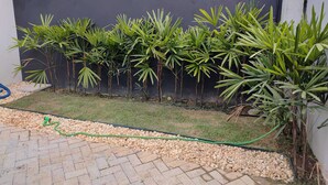 A garden with palm trees and a paved area in front of a dark wall. - Refuge 3 Indaiá Beach Bertioga 150 meters from the sea (Bertioga)