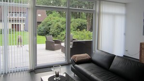A living room with a black leather sofa, a glass coffee table, and a view of a backyard through large sliding glass doors. - für 4 Personen ca. 165 m² in Mardorf, Niedersachsen (Steinhuder Meer) by Interhome (Mardorf)