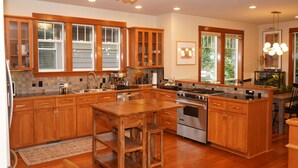 A spacious kitchen with wooden cabinets, a central island, stainless steel appliances, and large windows.