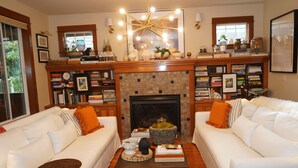 A living room with two white sofas, a fireplace, and a bookshelf filled with books.