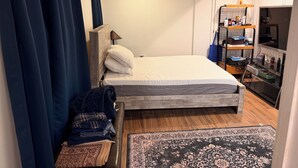 Quarto com cama, mesa de cabeceira, abajur, guarda-roupa e prateleira com diversos objetos.
