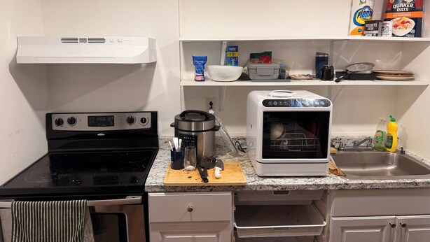 Uma cozinha equipada com fogão, forno, micro-ondas e pia. Inclui armários, bancada e diversos utensílios de cozinha, como uma cafeteira e uma chaleira.