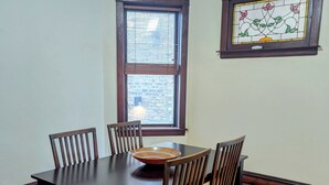 Een eetzaal met een donker houten tafel en stoelen, een glas-in-loodraam en een zichtbare bakstenen muur door het raam.