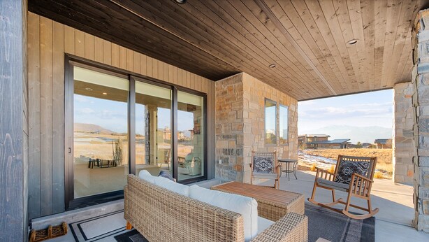 Un'area salotto esterna moderna con mobili in vimini e una poltrona a dondolo in legno, con vista su un paesaggio panoramico.