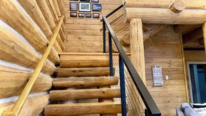 A wooden staircase with a metal railing, leading to a room with a wooden wall and framed pictures. - Walk to Lake, Downtown, Restaurants and Shops- Grand Mountain Haven (Grand Lake)
