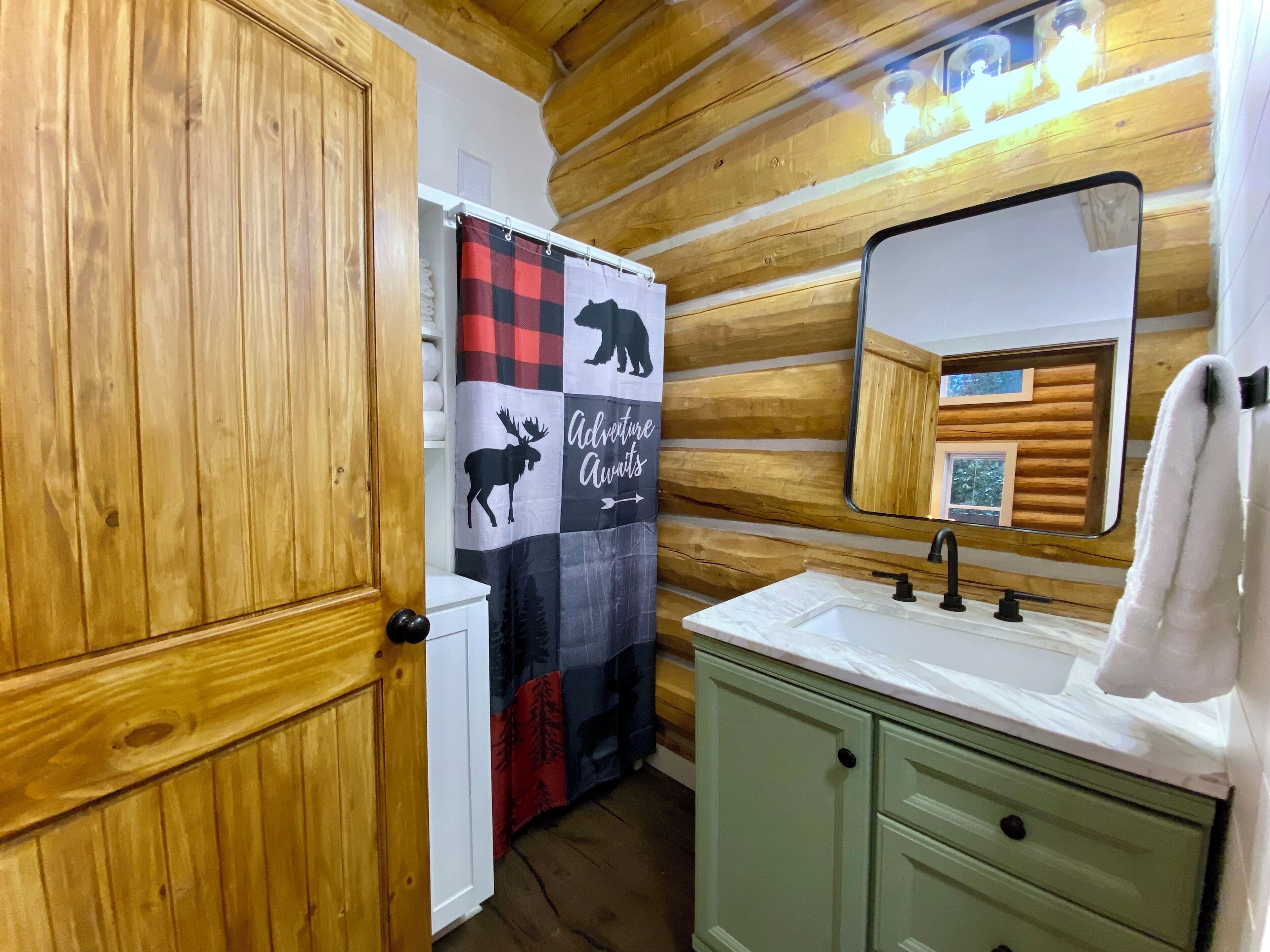 A bathroom with wooden walls, a checkered shower curtain, a mirror, and a sink.