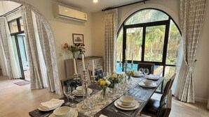 A dining area with a long table set for four, featuring white plates, glasses, and a vase with flowers. - Chivani modern private pool villa with garden in Na Jomtien Pattaya (Tambon Na Chom Thian)
