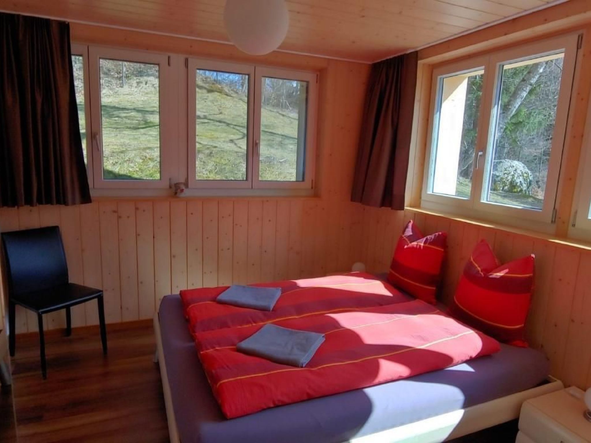 Un dormitorio con cama, una silla y ventanas amplias.