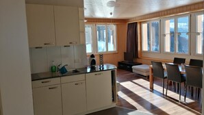 Cozinha moderna com armários brancos, sala de jantar com mesa e cadeiras de madeira, e janelas amplas com vista para o exterior.