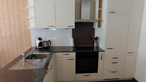 Cozinha com armários brancos, bancada preta, pia, fogão e luminária pendente.