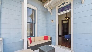 Un patio techado con un sofá color beige, una mesa de centro de vidrio y una silla azul.