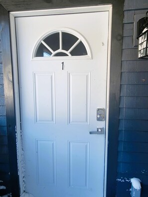 A white door with a number 1 above it, a small window above the door, and a doorbell. - H1 - Two-Bedroom Apartment (Lake Placid)