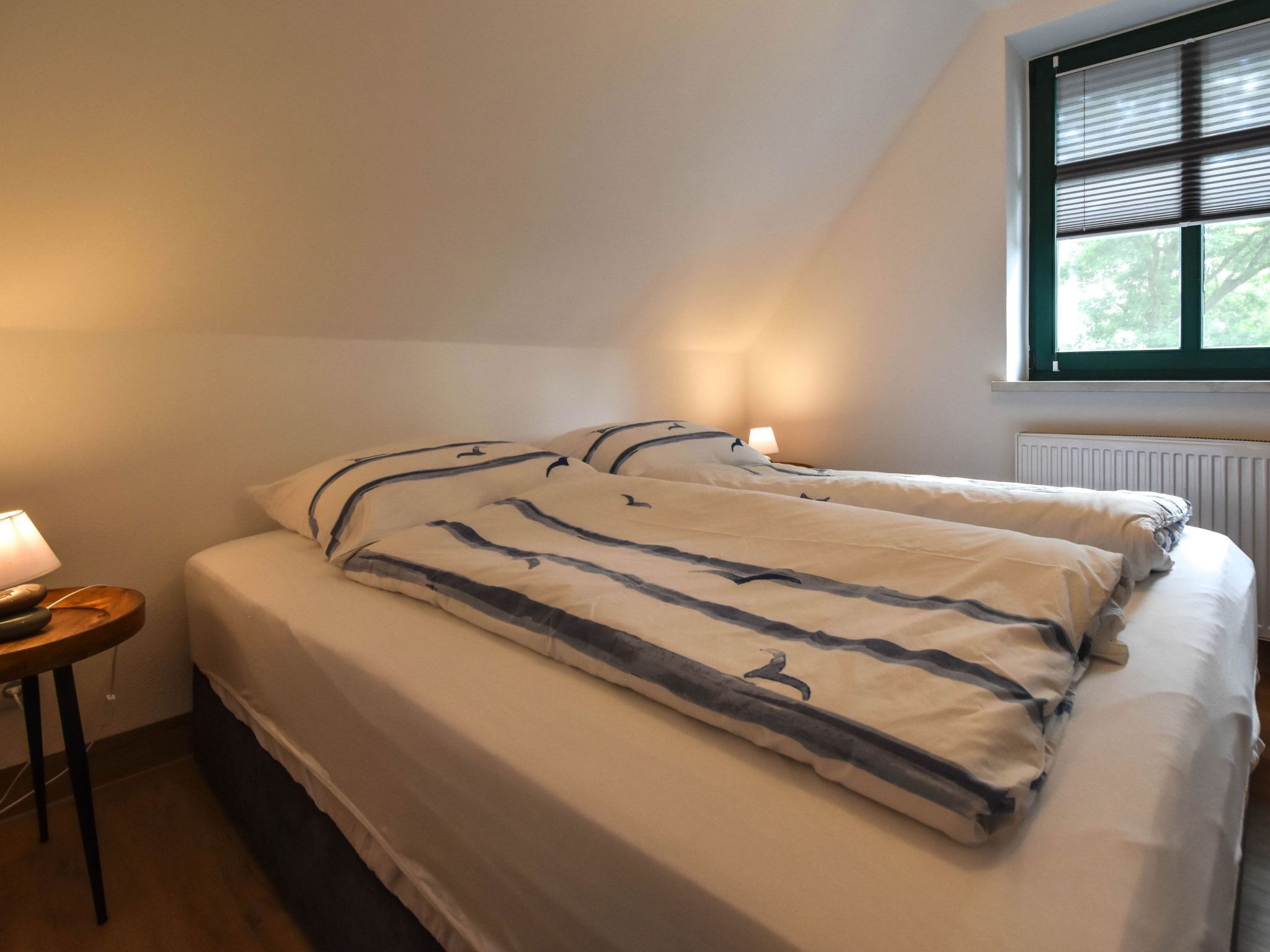 A bedroom with a bed, a nightstand, a lamp, and a window with blinds.