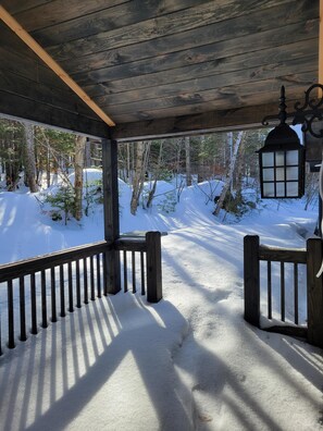 A wooden deck with a railing, a lantern, and a snowy landscape visible through the railing.
