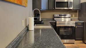 Une cuisine moderne dotée de plans de travail en granit, d’appareils électroménagers en acier inoxydable et de meubles de rangement aux couleurs sombres.