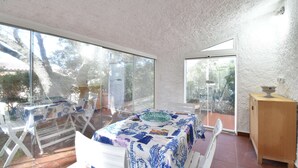 A room with a large glass door leading outside, a table with a blue and white tablecloth, and a wooden cabinet. - Detached cottage with a/c and two bathrooms (Aglientu)