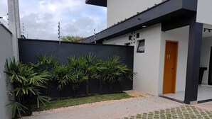 En moderne bygning med en sort facade, en dør og et belagt område med græs og beplantning.