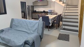 En moderne stue med sofa, spisebord med stole, et køkken og en trappe.