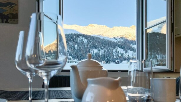 Ein Tisch mit Teekanne, Krug und zwei Weingläsern, mit Blick auf einen Berg durch ein Fenster.